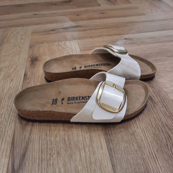 Madrid Big Buckle Le modèle BIRKENSTOCK Madrid est un grand classique qui s'est fait un nom dans l'univers de la mode grâce à son design épuré. Cette version Madrid Big Buckle associe deux designs très appréciés. Elle se présente avec un revêtement sobre à la brillance soyeuse et une grande et élégante boucle à ardillon. La matière extérieure se compose de Birko-Flor®, un matériau synthétique agréable sur la peau et résistant. SANDALES MADRID : LES ORIGINES DE BIRKENSTOCK L’histoire du modèle Madrid remonte aux années soixante, alors que BIRKENSTOCK lançait sur le marché ses sandales au design révolutionnaire. Celui-ci fut dévoilé au salon de la chaussure de 1963 à Düsseldorf... Mais ces sandales à une bride ne connurent d’abord pas un franc succès. Inspirées par l’esthétique audacieuse du brutalisme, avec leur lit de pied souple en liège et latex et leur bride unique ajustable, elles étaient trop avant-gardistes, notamment pour la mode de l’époque qui était alors aux talons aiguilles italiens, les stilettos. Mais il n’a pas fallu longtemps aux « sandales minceur » – ainsi nommées car elles favorisent l’activation du réflexe préhenseur des orteils lors de la marche, faisant ainsi travailler les muscles des pieds et des jambes – pour se faire apprécier du public. Plus de soixante ans plus tard, ce modèle désormais appelé Madrid est l’un de nos plus grands classiques et est resté peu ou prou fidèle à l’original. Sa popularité est une véritable preuve du caractère visionnaire des designs de BIRKENSTOCK.