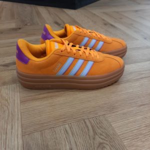 VL Court Bold Orange Une chaussure compensée au style polyvalent. Tout est une question d'équilibre avec cette chaussure adidas VL Court Bold Orange. Elle présente un design épuré, bien sûr, mais avec une semelle compensée qui sublime tout le look et te donne de la hauteur. La tige en cuir, la doublure textile et la semelle extérieure en caoutchouc résistant s'associent pour t'offrir un confort ultime au quotidien. La marque C'est le 18 août 1949 qu'Adi Dassler a démarré l'aventure adidas, avec pour objectif d'améliorer les performances des athlètes. 70 ans plus tard, adidas a laissé sa marque sur le monde du sport, mais aussi celui de la mode, de la musique, de la culture, du développement durable et bien d'autres encore. Voyage avec nous à travers le temps et découvre l'histoire d'adidas avec des modèles qui ont influencé le lifestyle d'aujourd'hui. Juste après la naissance officielle des 3 bandes en 1949, les années 50 ont connu un véritable boom technologique avec des équipements innovants pour les athlètes de classe mondiale. Ainsi, c'est pendant cette décennie qu'est apparue la Samba, toujours portée de nos jours pas les joueurs de Five et de futsal, et toujours présente dans la rue. Pendant les 50's, adidas a développé une chaussure de sprint qui a battu un record du monde et la première chaussure de football conçue avec une semelle en nylon, marquant une vraie nouveauté en termes de confort et de sensations. D'autres modèles ont vu le jour durant cette période, comme la chaussure de basketball Allround, devenue une véritable icône dans les 80's. Ces années ont été révolutionnaires, créant un véritable avant et après pour les sportifs de haut niveau. Mais ce n'était que le début de l'histoire d'adidas.