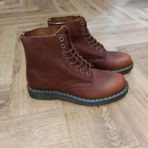 1460 Pascal Ambassador Nous avons repensé nos boots Dr. Martens 1460 Pascal Ambassador  plus souple au fini texturé. Ce modèle à 8 œillets est né le 1er avril 1960 et ultra-confortable à porter grâce à son cuir ultra-souple, durable et légèrement huilé qui s'embellit au fil du temps. Il présente aussi nos surpiqûres jaunes classiques et notre boucle d'enfilage jaune et noire au talon. Notre semelle à coussin d'air réputée vous permet de porter ces boots des heures durant en tout confort. Dr. Martens s'attache aux personnes qui ont leur propre style mais qui partagent un même esprit, des personnes authentiques qui représentent quelque chose de concret. Qui aiment s'exprimer honnêtement. Qui sont différentes. Sur un plan stylistique, les silhouettes épurées de Dr. Martens permettent à celles et ceux qui les portent de les intégrer à leur style individuel et unique. Sur un plan pratique, la solidité et le confort réputés de nos chaussures les rendent parfaites pour un quotidien partagé entre concert et mode urbaine. Et finalement, sur un plan émotionnel, elles sont une marque d'attitude et de confiance en soi. Mais ça n'a pas toujours été le cas. À l'origine, Dr. Martens proposait des boots de travail simples qui ont même brièvement été vendues comme des chaussures de jardinage. Donc comment est-ce que ces boots utilitaires sont devenues l'une des icônes culturelles les plus importantes de notre époque moderne ? C'est une histoire unique et intéressante...