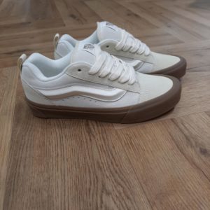 Knu Skool Beige: Un look contemporain inspiré du volume XXL des années 90  Les Knu Skool Beige en daim proposent une interprétation moderne d'un classique des années 90. En effet, elles se distinguent par leur languette rembourrée. Puis, elles possèdent une Sidestripe moulée 3D et des lacets épais oversize. Les Knu Skool s'émancipent des Old Skool originales, véritables icônes classiques. avec des tendances actuelles, une silhouette tapageuse et des finitions XXL. La marque C’est en 1966 que Paul, accompagné de son frère Jim et de ses amis Gordy et Serge, ouvre les portes de la Van Doren Rubber Company au 704 East Broadway à Anaheim, en Californie. Leur façon de travailler est alors unique, vendant leurs chaussures d’où elles sont fabriquées. « Des baskets en toile pour toute la famille » tel était le slogan qu’affichaient les boîtes à chaussures à l’époque. C’est le principe novateur de la Van Doren Rubber Company, fondée par ces deux frères originaires de Boston : produire à la commande et sur place, dans la petite usine qui jouxte les 40 m2 du magasin. Et vendre en direct cette chaussure en toile robuste reposant sur une semelle gaufrée en caoutchouc vulcanisé et antidérapante.  Hélas, cette sneaker disparaît brutalement des radars avec la faillite de Vans en 1983. Mais l’histoire de Vans n’écrivait pas son point final. Elle mettra vingt ans à redevenir le signe extérieur d’appartenance à la religion du cool, aux pieds des rockers, des grands ados et des stars d'Hollywood (Justin Bieber, Zac Efron, Harry Styles…). À bientôt 60 ans, cet indéboulonnable totem de la culture skate est aujourd’hui un classique du dressing estival porté flambant neuf à un mariage ou en fin de vie à la plage. Avant de les renouveler les yeux fermés…