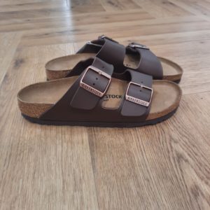 Arizona Dark Brown L'Arizona Dark Brown de BIRKENSTOCK est un grand classique qui séduit les hommes et les femmes depuis des décennies. Cette sobre sandale à deux brides est un parfait exemple de design intemporel. A ce titre, il y a bien longtemps qu’elle s’est imposée comme une chaussure confortable culte. Le dessus est en Birko-Flor®, une matière synthétique hypoallergénique et résistante. BIRKENSTOCK ARIZONA : LE MODÈLE TENDANCE ET CULTE Faites place aux Arizona – les sandales les plus populaires de BIRKENSTOCK. Depuis ses débuts en 1973, le modèle Arizona a conquis les cœurs et fait des millions d’adeptes dans le monde entier. Avec leur design intemporel et confortable, ces sandales sont toujours gage de style. Pour faire honneur à leur popularité, les Arizona ont été déclinées en plus de styles, de couleurs et de matières que n’importe quel autre modèle de BIRKENSTOCK, convenant à chaque occasion et à tous les goûts. Plus que tout autre modèle, les sandales Arizona ont contribué à façonner l’image de BIRKENSTOCK. D’ailleurs, nous parions que lorsque vous pensez à BIRKENSTOCK, ce sont les Arizona qui vous viennent d’emblée à l’esprit. Iconique, ce modèle représente BIRKENSTOCK dans toute son essence. En presque un demi-siècle, le design emblématique a à peine changé en matière de style ou de fonctionnalité. Pourtant, sa popularité n’a pas diminué d’un iota. Une vraie preuve de la renommée et de l’appréciation de ce modèle.