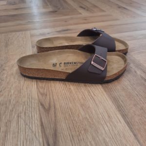 Madrid Dark Brown Aîné de la famille, le modèle BIRKENSTOCK Madrid Dark Brown est un vrai classique. Lancées il y a une cinquantaine d'années comme des « sandales de gymnastique », ces sandales à une bride épurées se sont peu à peu imposées comme un véritable compagnon de mode. Le dessus est en Birko-Flor®, une matière synthétique hypoallergénique et résistante. SANDALES MADRID : LES ORIGINES DE BIRKENSTOCK L’histoire du modèle Madrid remonte aux années soixante, alors que BIRKENSTOCK lançait sur le marché ses sandales au design révolutionnaire. Celui-ci fut dévoilé au salon de la chaussure de 1963 à Düsseldorf... Mais ces sandales à une bride ne connurent d’abord pas un franc succès. Inspirées par l’esthétique audacieuse du brutalisme, avec leur lit de pied souple en liège et latex et leur bride unique ajustable, elles étaient trop avant-gardistes, notamment pour la mode de l’époque qui était alors aux talons aiguilles italiens, les stilettos. Mais il n’a pas fallu longtemps aux « sandales minceur » – ainsi nommées car elles favorisent l’activation du réflexe préhenseur des orteils lors de la marche, faisant ainsi travailler les muscles des pieds et des jambes – pour se faire apprécier du public. Plus de soixante ans plus tard, ce modèle désormais appelé Madrid est l’un de nos plus grands classiques et est resté peu ou prou fidèle à l’original. Sa popularité est une véritable preuve du caractère visionnaire des designs de BIRKENSTOCK.