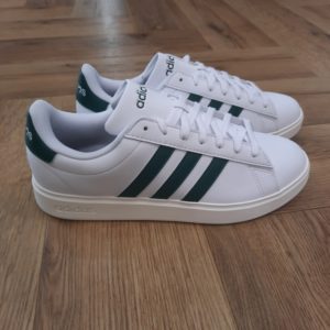 Adidas Grand Court 2.0-Chaussures adidas Grand Court 2.0 blanc intense vert-L'histoire des logos adidas commence avec la naissance de la marque adidas. Au moment de sa création par Adolf Dassler en 1949, adidas ne fabriquait que des chaussures de sport. Rien de surprenant, donc, à ce que le logo adidas ne mette que cet élément en avant. Le tout premier logo représentait en effet une chaussure d'athlétisme à crampons, ornée bien évidemment des 3 bandes signature, trônant entre les deux « d » d'adidas aux barres rallongées. « Sportschuhe » (« chaussures de sport » en allemand) est inscrit sous adidas, et ce logo était souvent présenté dans un bleu aujourd'hui classique pour la marque.