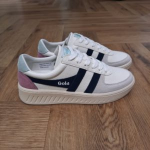 Gola Grandslam Trident Découvrez les Gola Grandslam Trident, des baskets tendance qui allient style et confort. Conçues pour les femmes modernes, ces chaussures blanches avec des touches de bleu marine s'adaptent à toutes vos tenues, que ce soit pour une promenade en ville ou pour une sortie décontractée entre amis. Avec leur design élégant et leur matériau de qualité, elles sont parfaites pour toutes les saisons, assurant un look frais et contemporain en toute occasion. La marque Gola est une marque principalement connue pour ses chaussures de sport. Elle a été créé en 1905 à Leicester, au Royaume Uni. Pour l'anecdote, personne ne sait exactement d'où vient le nom de la marque. Pourtant, une légende urbaine raconte qu'elle doit son nom à l'anagramme du mot "Goal" (qui signifie "but" en anglais). La marque commence à être connue à la fin des années 1960. Notamment dans le sport notamment avec la Harrier qui reste aujourd'hui encore le modèle phare de la marque anglaise. En effet, elle a très vite été adoptée par le grand public. Fort de son histoire, la marque a su traverser les générations et est aujourd'hui une marque streetwear à part entière qui sait innover et suivre les tendances. On a d'ailleurs pu voir une collection 100 % vegan sortir des tuyaux en 2019, preuve de la capacité de Gola à s'adapter au marché actuel !