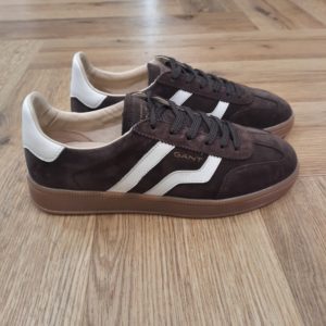 Gant Cuzima Marron La chaussure Gant Cuzima Marron est une paire de baskets d'inspiration rétro, qui se porte en toute saison. Tout d'abord, elles sont dotées d'une tige en cuir de qualité supérieure. De plus, elles arborent des finitions de couleur contrastante au niveau du bout, du talon et sur le côté. Puis, sa fine semelle extérieure en caoutchouc et la doublure en coton éponge apportent un style vintage à l'ensemble. Les baskets Gant Cuzima pour femme sont la fusion parfaite entre style rétro et confort. Avec leur design intemporel et leurs matériaux de qualité supérieure, elles sont idéales pour toute occasion. Elles garantissent un look décontracté et moderne qui ne passera pas inaperçu. La marque Quand Bernard Gant, un immigrant ukrainien, arrive à New-York en 1914, il se plonge directement au cœur des métiers du prêt-à-porter. Il travaille dans un atelier de confection de chemises dans le centre de la ville. Ce n'est que quelques années plus tard, alors qu'il a déménagé à New Haven dans le Connecticut qu'il lancera l'entreprise familiale à l'aide de sa femme, également dans le métier. Rapidement, il fabrique des chemises pour les plus grandes marques du pays tel que Brooks Brothers. Si le style de Gant a beaucoup évolué au cours des années, il ne s'est jamais vraiment détaché de son image de marque Américaine traditionnelle. En effet, adepte du style Ivy avec comme produit phare la chemise à col boutonné. Après avoir été suédoise, la marque a été rachetée en 2008 par le groupe suisse Maus Frères, qui détient entre autres Lacoste et Aigle, mais elle garde encore ses valeurs originelles : celles de Bernard Gant.