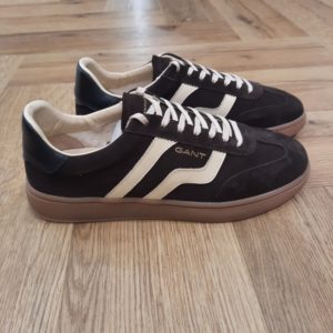 Gant Cuzmo Chocolat Les baskets Gant Cuzmo Chocolat sont fabriquées avec des matériaux de qualité supérieure qui reflètent l'essence du meilleur American Sportswear. Pour commencer, ce modèle se distingue par sa construction en daim doux, qui offre une finition élégante et durable. Puis, son design à silhouette basse, complété par une semelle en caoutchouc, garantit un ajustement confortable et sûr. Les semelles aux tons miel et les accents de couleurs contrastantes sur les côtés et à l'arrière ajoutent une touche moderne et distinctive. Elles sont idéales pour un look décontracté et urbain. En effet, ces baskets s'adaptent à différents styles, devenant une option polyvalente pour toute garde-robe. La marque Quand Bernard Gant, un immigrant ukrainien, arrive à New-York en 1914, il se plonge directement au cœur des métiers du prêt-à-porter. Il travaille dans un atelier de confection de chemises dans le centre de la ville. Ce n'est que quelques années plus tard, qu'il lancera l'entreprise familiale à l'aide de sa femme, également dans le métier. Rapidement, il fabrique des chemises pour les plus grandes marques du pays tel que Brooks Brothers. Si le style de Gant a beaucoup évolué au cours des années, il ne s'est jamais vraiment détaché de son image de marque Américaine traditionnelle. En effet, adepte du style Ivy avec comme produit phare la chemise à col boutonné. Après avoir été suédoise, la marque a été rachetée en 2008 par le groupe suisse Maus Frères, qui détient entre autres Lacoste et Aigle, mais elle garde encore ses valeurs originelles : celles de Bernard Gant.