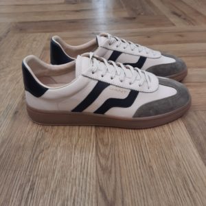 Gant Cuzmo Beige Les baskets Gant Cuzmo Beige sont fabriquées avec des matériaux de qualité supérieure qui reflètent l'essence du meilleur American Sportswear. Pour commencer, ce modèle se distingue par sa construction en daim doux, qui offre une finition élégante et durable. Puis, son design à silhouette basse, complété par une semelle en caoutchouc, garantit un ajustement confortable et sûr. Les semelles aux tons miel et les accents de couleurs contrastantes sur les côtés et à l'arrière ajoutent une touche moderne et distinctive. Elles sont idéales pour un look décontracté et urbain. En effet, ces baskets s'adaptent à différents styles, devenant une option polyvalente pour toute garde-robe. La marque Quand Bernard Gant, un immigrant ukrainien, arrive à New-York en 1914, il se plonge directement au cœur des métiers du prêt-à-porter. Il travaille dans un atelier de confection de chemises dans le centre de la ville. Ce n'est que quelques années plus tard, qu'il lancera l'entreprise familiale à l'aide de sa femme, également dans le métier. Rapidement, il fabrique des chemises pour les plus grandes marques du pays tel que Brooks Brothers. Si le style de Gant a beaucoup évolué au cours des années, il ne s'est jamais vraiment détaché de son image de marque Américaine traditionnelle. En effet, adepte du style Ivy avec comme produit phare la chemise à col boutonné. Après avoir été suédoise, la marque a été rachetée en 2008 par le groupe suisse Maus Frères, qui détient entre autres Lacoste et Aigle, mais elle garde encore ses valeurs originelles : celles de Bernard Gant.