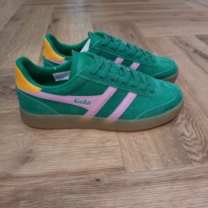 Gola Viper Green  Avec ses racines remontant au design Gola de 1976, la Gola Viper Green associe une tige courte et élégante à bout en T et une semelle à sept œillets. Cette association donne naissance à une basket classique aux proportions parfaites. En effet, celle ci est agrémentée d'une semelle en gomme tendance. On adore les lignes minimalistes de cette basket femme en daim moelleux, présentée ici en prune avec une bordure Wingflash Gola bleu Pacifique et un talon jaune pollen. La Viper nous transporte à l'âge d'or de Gola. La marque Gola est une marque principalement connue pour ses chaussures de sport. Elle a été créé en 1905 à Leicester, au Royaume Uni. Pour l'anecdote, personne ne sait exactement d'où vient le nom de la marque. Pourtant, une légende urbaine raconte qu'elle doit son nom à l'anagramme du mot "Goal" (qui signifie "but" en anglais). La marque commence à être connue à la fin des années 1960. Notamment dans le sport notamment avec la Harrier qui reste aujourd'hui encore le modèle phare de la marque anglaise. En effet, elle a très vite été adoptée par le grand public. Fort de son histoire, la marque a su traverser les générations et est aujourd'hui une marque streetwear à part entière qui sait innover et suivre les tendances. On a d'ailleurs pu voir une collection 100 % vegan sortir des tuyaux en 2019, preuve de la capacité de Gola à s'adapter au marché actuel !