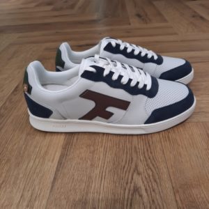 Faguo Hazel White Navy La Faguo Hazel White Navy est une basket basse inspirée des baskets des années 80. D'abord, sa semelle cousue à la tige a été pensée dans notre studio pour une durée de vie optimale. Puis, reconnaissable grâce à son logo F sur le côté, elle est l'incontournable FAGUO à porter pour toutes les occasions. FAGUO est certifié B Corp™ pour garantir des standards sociaux et environnementaux élevés et une transparence totale. Cette pièce FAGUO a été conçue à Nantes en France et fabriquée dans un atelier au Vietnam audité en externe pour valider ses bonnes pratiques sociales et environnementales. La marque Faguo est une marque française créée en 2009 par Frédéric Mugnier et Nicolas Rohr, alors qu'ils étaient encore étudiants et seulement âgés de 22 ans. C'est au cours d'un voyage universitaire en Chine qu'ils vont concevoir le projet Faguo. Il s'agit d'ailleurs d'un nom chinois signifiant tout simplement "France". Dans une démarche de responsabilité sociale et environnementale, ils vont imaginer le principe suivant : pour chaque produit Faguo acheté, un arbre sera planté en France. Et ce premier produit sera une simple tennis en toile ornée d'un bouton en noix de coco, représentant cet engagement. Leur concept va connaître un véritable succès qui va mener la marque à lancer de nouveaux modèles.