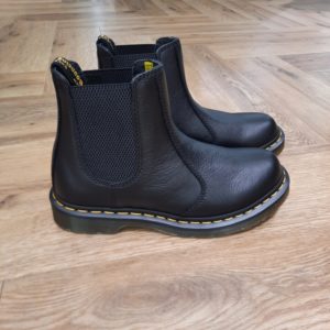 2976 Virginia Black Nous avons repensé nos très populaires Chelsea boots 2976 en cuir Virginia, un matériau texturé au toucher doux qui se fera encore plus vite au pied. La semelle est soulignée de nos surpiqûres jaunes classiques, ainsi que de nos rayures signature. Retrouvez de plus notre languette jaune et noire au talon. The History of Dr. Martens Dr. Martens s'attache aux personnes qui ont leur propre style mais qui partagent un même esprit, des personnes authentiques qui représentent quelque chose de concret. Qui aiment s'exprimer honnêtement. Qui sont différentes. Sur un plan stylistique, les silhouettes épurées de Dr. Martens permettent à celles et ceux qui les portent de les intégrer à leur style individuel et unique. Sur un plan pratique, la solidité et le confort réputés de nos chaussures les rendent parfaites pour un quotidien partagé entre concert et mode urbaine. Et finalement, sur un plan émotionnel, elles sont une marque d'attitude et de confiance en soi. Mais ça n'a pas toujours été le cas. À l'origine, Dr. Martens proposait des boots de travail simples qui ont même brièvement été vendues comme des chaussures de jardinage. Donc comment est-ce que ces boots utilitaires sont devenues l'une des icônes culturelles les plus importantes de notre époque moderne ? C'est une histoire unique et intéressante...