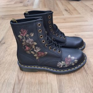 1460 Decayed Roses Cette nouvelle version de nos boots 1460 à 8 œillets combine roses fanées et cuir Classic Tumbled Nappa texturé. D'abord, ces chaussures sont dotées de finitions en cuir vieilli pour accentuer l'allure vintage. Puis, elles reposent sur notre semelle Doc's renforcée de nos surpiqûres jaunes signature. L'histoire Dr Martens En 1945, Klaus Maertens, un médecin allemand, crée ces chaussures à la suite d’un accident de ski. Des chaussures avec une semelle soudée. C’est une soudure à chaud qui permet d’emprisonner l’air, et c’est ce qui fait qu’elle sera très confortable et va devenir au début, une chaussure orthopédique. Pour fabriquer la semelle, Klaus Maertens récupère le caoutchouc des avions militaires abandonnés dans les hangars, le métal des vestes des soldats pour faire les œillets de la botte, et le cuir sur certains de leurs pantalons. Le succès est immédiat en 1947. Grâce à ces chaussures, les gens peuvent marcher dans des rues souvent détruites par la guerre. La compagnie ouvre une usine à Munich en 1952 et crée déjà 200 styles différents de chaussures. Cette invention allemande est adoptée en Angleterre lorsque Bill Griggs remarque ce modèle de chaussure, achète la licence et l’améliore. Il bombe l’avant et va faire cette fameuse semelle à rainures qui est transparente, qui permet de voir un peu où se cache l’air dans la chaussure. Aussi, d’avoir cette fameuse couture jaune permet de la reconnaître immédiatement de très loin. Les ouvriers, les policiers, les postiers, le personnel des hôpitaux et les cols bleus se mettent à porter des Dr. Martens. Plus tard, les skinheads ainsi que des groupes radicaux et racistes les portent pour afficher leur révolte contre la société.