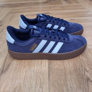 Adidas VL Court Bleu Cette sneaker Adidas VL Court Bleu est à la fois simple et audacieuse. En effet, elle est conçue en cuir souple et doublée pour plus de confort. D'abord, son amorti léger t'offre le maintien dont tu as besoin pendant les journées actives. Puis, elle possède une semelle extérieure en caoutchouc vulcanisé pour plus de souplesse et un style d'inspiration skate.  La marque C'est le 18 août 1949 qu'Adi Dassler a démarré l'aventure adidas, avec pour objectif d'améliorer les performances des athlètes. 70 ans plus tard, adidas a laissé sa marque sur le monde du sport, mais aussi celui de la mode, de la musique, de la culture, du développement durable et bien d'autres encore. Voyage avec nous à travers le temps et découvre l'histoire d'adidas avec des modèles qui ont influencé le lifestyle d'aujourd'hui. Juste après la naissance officielle des 3 bandes en 1949, les années 50 ont connu un véritable boom technologique avec des équipements innovants pour les athlètes de classe mondiale. Ainsi, c'est pendant cette décennie qu'est apparue la Samba, toujours portée de nos jours pas les joueurs de Five et de futsal, et toujours présente dans la rue. Pendant les 50's, adidas a développé une chaussure de sprint qui a battu un record du monde et la première chaussure de football conçue avec une semelle en nylon, marquant une vraie nouveauté en termes de confort et de sensations. D'autres modèles ont vu le jour durant cette période, comme la chaussure de basketball Allround, devenue une véritable icône dans les 80's. Ces années ont été révolutionnaires, créant un véritable avant et après pour les sportifs de haut niveau. Mais ce n'était que le début de l'histoire d'adidas.