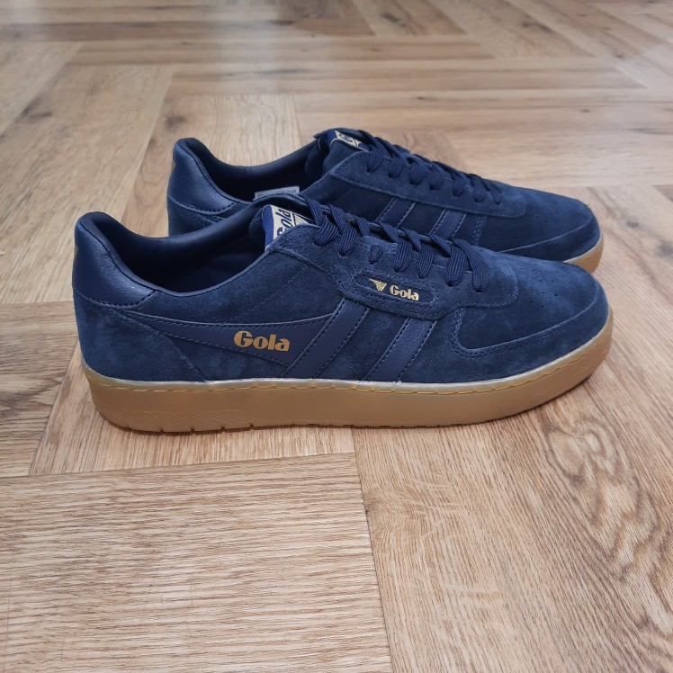 Gola Hawk Navy La toute nouvelle Gola Hawk Navy rejoint la gamme emblématique. En effet, le modèle authentique Hawk est revisité avec une tige en daim de qualité couleur tabac et une semelle en gomme. Tout d'abord, son style chaleureux et décontracté dégage une touche vintage. En effet, c'est le complément idéal de toute garde-robe, pour un usage quotidien et pour donner du caractère à toutes vos tenues. La marque Gola est une marque principalement connue pour ses chaussures de sport. Elle a été créé en 1905 à Leicester, au Royaume Uni. Pour l'anecdote, personne ne sait exactement d'où vient le nom de la marque. Pourtant, une légende urbaine raconte qu'elle doit son nom à l'anagramme du mot "Goal" (qui signifie "but" en anglais). La marque commence à être connue à la fin des années 1960. Notamment dans le sport notamment avec la Harrier qui reste aujourd'hui encore le modèle phare de la marque anglaise. En effet, elle a très vite été adoptée par le grand public. Fort de son histoire, la marque a su traverser les générations et est aujourd'hui une marque streetwear à part entière qui sait innover et suivre les tendances. On a d'ailleurs pu voir une collection 100 % vegan sortir des tuyaux en 2019, preuve de la capacité de Gola à s'adapter au marché actuel !