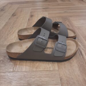 Arizona Concrete Gray L'Arizona Concrete Gray de BIRKENSTOCK est un grand classique qui séduit les hommes et les femmes depuis des décennies. La sandale ajustable de manière individuelle au moyen de ses deux brides s'est depuis longtemps imposée comme une chaussure culte. La matière extérieure se compose de cuir naturel souple de qualité supérieure. L’histoire de Birkenstock Tout commence en 1774, lorsque Johann Adam Birkenstock, un cordonnier allemand passionné, fonde ce qui allait devenir l'une des marques de chaussures les plus emblématiques au monde. À l'époque, Johann menait une petite entreprise modeste qui lui permettait de vivre confortablement. Mais comment cette production familiale a-t-elle pu se transformer en un empire mondial de la chaussure ? Le tournant se produit en 1896 avec Konrad Birkenstock, un descendant de la famille. Konrad, visionnaire, décide de donner un coup de jeune à l'entreprise familiale. C'est lui qui a développé la première semelle intérieure orthopédique, une innovation qui a littéralement mis le sabot Birkenstock sur la carte mondiale. Cependant, il aura fallu plusieurs générations et une évolution constante pour que Birkenstock devienne la marque internationale que l'on connaît aujourd'hui. Le grand bond en avant s’est produit au XXe siècle, notamment aux États-Unis dans les années 1960, où les sandales Birkenstock sont devenues un symbole de la contre-culture et du confort.