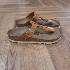 Gizeh Braided Cognac Le modèle Gizeh Braided Cognac, un des grands classiques de la marque, affiche un design minimaliste tendance, tout en offrant un maintien parfait. Cette chaussure arbore ici un détail particulier : des brides tressées, qui se marient parfaitement à un style bohème actuel. Côté composition, sa tige a été confectionnée dans un cuir nubuck huilé particulièrement épais, à bords bruts. L’histoire de Birkenstock Tout commence en 1774, lorsque Johann Adam Birkenstock, un cordonnier allemand passionné, fonde ce qui allait devenir l'une des marques de chaussures les plus emblématiques au monde. À l'époque, Johann menait une petite entreprise modeste qui lui permettait de vivre confortablement. Mais comment cette production familiale a-t-elle pu se transformer en un empire mondial de la chaussure ? Le tournant se produit en 1896 avec Konrad Birkenstock, un descendant de la famille. Konrad, visionnaire, décide de donner un coup de jeune à l'entreprise familiale. C'est lui qui a développé la première semelle intérieure orthopédique, une innovation qui a littéralement mis le sabot Birkenstock sur la carte mondiale. Cependant, il aura fallu plusieurs générations et une évolution constante pour que Birkenstock devienne la marque internationale que l'on connaît aujourd'hui. Le grand bond en avant s’est produit au XXe siècle, notamment aux États-Unis dans les années 1960, où les sandales Birkenstock sont devenues un symbole de la contre-culture et du confort.