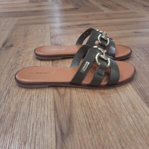 Hamia Kaki Découvrez le modèle Hamia Kaki, une mule élégante qui incarne parfaitement le style et la sophistication. Imaginez-vous glisser vos pieds dans ces mules au cuir souple. Elles sont parfaites pour accompagner vos journées en ville ou vos promenades en bord de mer. En effet, elles allient confort et chic grâce à une conception minutieuse qui soutient chaque pas avec légèreté. Les mules Hamia sont pensées pour la femme indépendante et solaire. Celle qui arbore avec assurance un look à la fois raffiné et urbain. De plus, leur design intemporel et polyvalent se marie aisément avec une robe estivale légère ou un pantalon de lin. Ceci ajoutant une touche de raffinement à votre silhouette. Chaque détail est soigneusement étudié pour vous offrir une expérience sensorielle unique, alors que le cuir caresse délicatement votre peau. En optant pour les mules Hamia, vous choisissez un allié de choix pour sublimer votre allure, jour après jour. Les Tropeziennes par M. Belarbi : L’histoire d’un style intemporel, né à Saint-Tropez Mo Belarbi, né à Fez, est un créateur visionnaire et passionné par le cuir, l’artisanat et les voyages. En 1975 dans le village emblématique de Saint-Tropez dont il tombe amoureux, il ouvre son premier concept store «La Puce Tropezienne», un lieu unique, foisonnant de créativité et d’audace. Mo Belarbi, esprit libre et innovant y imagine des modèles qui deviendront iconiques, intergénérationnels et s’imposeront rapidement comme incontournables.