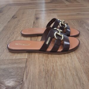 Hamia Chocolat Découvrez le modèle Hamia Chocolat, une mule élégante qui incarne parfaitement le style et la sophistication. Pour commencer, imaginez-vous glisser vos pieds dans ces mules au cuir souple. En effet, elles sont parfaites pour accompagner vos journées en ville ou vos promenades en bord de mer. De plus, elles allient confort et chic grâce à une conception minutieuse qui soutient chaque pas avec légèreté. Les mules Hamia sont pensées pour la femme indépendante et solaire. Celle qui arbore avec assurance un look à la fois raffiné et urbain. De plus, leur design intemporel et polyvalent se marie aisément avec une robe estivale légère ou un pantalon de lin. Chaque détail est soigneusement étudié pour vous offrir une expérience sensorielle unique. En optant pour les mules Hamia, vous choisissez un allié de choix pour sublimer votre allure, jour après jour. Les Tropeziennes par M. Belarbi : L’histoire d’un style intemporel, né à Saint-Tropez Mo Belarbi, né à Fez, est un créateur visionnaire et passionné par le cuir, l’artisanat et les voyages. En 1975 dans le village emblématique de Saint-Tropez dont il tombe amoureux, il ouvre son premier concept store «La Puce Tropezienne», un lieu unique, foisonnant de créativité et d’audace. Mo Belarbi, esprit libre et innovant y imagine des modèles qui deviendront iconiques, intergénérationnels et s’imposeront rapidement comme incontournables.