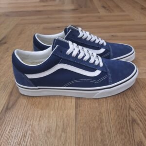 Old Skool Bleu Cette sneaker emblématique Old Skool Bleu séduit par son design intemporel et sa robustesse légendaire. Le contraste saisissant de son empeigne en toile et cuir affiche une identité forte, relevée par la fameuse bande latérale blanche. La Old Skool a été notre première chaussure à porter la célèbre Sidestripe de Vans, même s’il ne s’agissait à l’époque que d’un simple griffonnage dessiné par le fondateur Paul Van Doren. Ces chaussures basses se sont imposées dès leur début en 1977 comme une icône dans les milieux du skate, de la musique et de la mode. Des punks aux fans de skate des années 90, en passant par les légendes de la mode et du hip-hop d’aujourd’hui, la Old Skool en toile a toujours été une référence pour les esprits libres et créatifs. La création de Vans L’histoire de Vans débute en 1966, lorsqu’un certain Paul Van Doren, accompagné de son frère Jim Van Doren et de deux associés, Gordon Lee et Serge Delia, décide d’ouvrir un magasin de chaussures à Anaheim, en Californie. Contrairement aux autres fabricants de chaussures de l’époque, Vans adopte un concept novateur : elle fabrique et vend directement ses propres produits, supprimant ainsi les intermédiaires. La première boutique propose alors un modèle unique, sobrement appelé « Vans #44 Deck Shoes », qui deviendra plus tard la célèbre Authentic. Très vite, la marque attire l’attention des skateurs californiens, séduits par l’adhérence exceptionnelle de la semelle en caoutchouc gaufré et la robustesse des chaussures. Le bouche-à-oreille fonctionne et Vans devient rapidement une référence incontournable dans le monde du skateboard, un sport encore en plein essor à cette époque. Grâce à cette popularité naissante, l’entreprise commence à développer de nouveaux modèles et à se diversifier, jusqu’à devenir l’icône que l’on connaît aujourd’hui