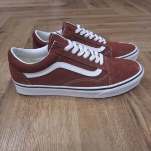 Old Skool Brique Cette sneaker emblématique Old Skool Brique séduit par son design intemporel et sa robustesse légendaire. Le contraste saisissant de son empeigne en toile et cuir affiche une identité forte, relevée par la fameuse bande latérale blanche. La Old Skool a été notre première chaussure à porter la célèbre Sidestripe de Vans, même s’il ne s’agissait à l’époque que d’un simple griffonnage dessiné par le fondateur Paul Van Doren. Ces chaussures basses se sont imposées dès leur début en 1977 comme une icône dans les milieux du skate, de la musique et de la mode. Des punks aux fans de skate des années 90, en passant par les légendes de la mode et du hip-hop d’aujourd’hui, la Old Skool en toile a toujours été une référence pour les esprits libres et créatifs. La création de Vans L’histoire de Vans débute en 1966, lorsqu’un certain Paul Van Doren, accompagné de son frère Jim Van Doren et de deux associés, Gordon Lee et Serge Delia, décide d’ouvrir un magasin de chaussures à Anaheim, en Californie. Contrairement aux autres fabricants de chaussures de l’époque, Vans adopte un concept novateur : elle fabrique et vend directement ses propres produits, supprimant ainsi les intermédiaires. La première boutique propose alors un modèle unique, sobrement appelé « Vans #44 Deck Shoes », qui deviendra plus tard la célèbre Authentic. Très vite, la marque attire l’attention des skateurs californiens, séduits par l’adhérence exceptionnelle de la semelle en caoutchouc gaufré et la robustesse des chaussures. Le bouche-à-oreille fonctionne et Vans devient rapidement une référence incontournable dans le monde du skateboard, un sport encore en plein essor à cette époque. Grâce à cette popularité naissante, l’entreprise commence à développer de nouveaux modèles et à se diversifier, jusqu’à devenir l’icône que l’on connaît aujourd’hui