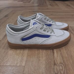 vans rowley beige-Chaussures Rowley Classic-Sneakers ROWLEY VANS Homme Beige-L’histoire de Vans débute en 1966, lorsqu’un certain Paul Van Doren, accompagné de son frère Jim Van Doren et de deux associés, Gordon Lee et Serge Delia, décide d’ouvrir un magasin de chaussures à Anaheim, en Californie. Contrairement aux autres fabricants de chaussures de l’époque, Vans adopte un concept novateur : elle fabrique et vend directement ses propres produits, supprimant ainsi les intermédiaires. La première boutique propose alors un modèle unique, sobrement appelé « Vans #44 Deck Shoes », qui deviendra plus tard la célèbre Authentic. Très vite, la marque attire l’attention des skateurs californiens, séduits par l’adhérence exceptionnelle de la semelle en caoutchouc gaufré et la robustesse des chaussures. Le bouche-à-oreille fonctionne et Vans devient rapidement une référence incontournable dans le monde du skateboard, un sport encore en plein essor à cette époque. Grâce à cette popularité naissante, l’entreprise commence à développer de nouveaux modèles et à se diversifier, jusqu’à devenir l’icône que l’on connaît aujourd’hui.