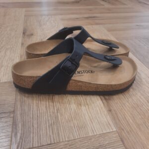 Gizeh Cuir Black Grand classique BIRKENSTOCK, la Gizeh Cuir Black est une chaussure stylée multitalent. En effet, notre élégante sandale à entre-doigts affiche un design minimaliste tendance, tout en offrant un maintien parfait. De plus, sa tige se compose de cuir naturel souple de qualité supérieure. L’histoire de Birkenstock Tout commence en 1774, lorsque Johann Adam Birkenstock, un cordonnier allemand passionné, fonde ce qui allait devenir l'une des marques de chaussures les plus emblématiques au monde. À l'époque, Johann menait une petite entreprise modeste qui lui permettait de vivre confortablement. Mais comment cette production familiale a-t-elle pu se transformer en un empire mondial de la chaussure ? Le tournant se produit en 1896 avec Konrad Birkenstock, un descendant de la famille. Konrad, visionnaire, décide de donner un coup de jeune à l'entreprise familiale. C'est lui qui a développé la première semelle intérieure orthopédique, une innovation qui a littéralement mis le sabot Birkenstock sur la carte mondiale. Cependant, il aura fallu plusieurs générations et une évolution constante pour que Birkenstock devienne la marque internationale que l'on connaît aujourd'hui. Le grand bond en avant s’est produit au XXe siècle, notamment aux États-Unis dans les années 1960, où les sandales Birkenstock sont devenues un symbole de la contre-culture et du confort.