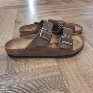 Arizona Dark Tea L’Arizona, classique BIRKENSTOCK au design intemporel, comble hommes et femmes depuis des décennies. Sur la sandale Arizona Dark Tea, les détails et les boucles de couleur assortie au toucher textile d’aspect mat lui confèrent une petite touche d’originalité supplémentaire. Sa tige se compose de cuir velours doux. L’histoire de Birkenstock Tout commence en 1774, lorsque Johann Adam Birkenstock, un cordonnier allemand passionné, fonde ce qui allait devenir l'une des marques de chaussures les plus emblématiques au monde. À l'époque, Johann menait une petite entreprise modeste qui lui permettait de vivre confortablement. Mais comment cette production familiale a-t-elle pu se transformer en un empire mondial de la chaussure ? Le tournant se produit en 1896 avec Konrad Birkenstock, un descendant de la famille. Konrad, visionnaire, décide de donner un coup de jeune à l'entreprise familiale. C'est lui qui a développé la première semelle intérieure orthopédique, une innovation qui a littéralement mis le sabot Birkenstock sur la carte mondiale. Cependant, il aura fallu plusieurs générations et une évolution constante pour que Birkenstock devienne la marque internationale que l'on connaît aujourd'hui. Le grand bond en avant s’est produit au XXe siècle, notamment aux États-Unis dans les années 1960, où les sandales Birkenstock sont devenues un symbole de la contre-culture et du confort.