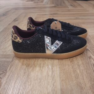 Berlin Ciclista Paillettes Baskets fabriquées en Espagne en glitter texturé avec empiècements en daim pour femme. V de victoria latérale métallisée et détail animal print sur la pièce arrière (en coloris noir et kaki). Nouveau bout type cycliste. Fermeture avec lacets épais ton sur ton et animal print (en coloris argent). Languette recouverte d'un tissu effet moutonné (en coloris noir et marron). Semelle en T.R. translucide coloris caramel. La marque Victoria est une marque qui a vu le jour en 1915 en Espagne. Le fondateur de la marque a commencé l'aventure avec une petite tennis qu'il a nommée comme sa femme adorée. Les chaussures Victoria ont évolué avec le temps bien sûr mais la marque s'évertue à conserver son ADN. Les Victoria évoluent et se parent de nouvelles couleurs, de matières originales ou d'imprimés, mais la base de la chaussure reste la même pour le plus grand plaisir des fans de la première heure. Les designers proposent de vastes collections chaque année qui renouvelle l'essence de Victoria ce qui lui permet de rester parmi les marques favorites des Espagnoles.