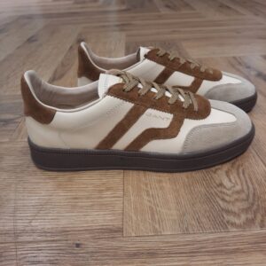 Cuzima Cream Nut Cuzima Cream Nut est un modèle d’inspiration rétro, qui se porte en toute saison. Tout d'abord, ces chaussures conçues avec une tige en cuir se distinguent par des finitions en daim lisse sur les côtés et au niveau du contrefort. Puis, la semelle extérieure en caoutchouc thermoplastique, associée à une doublure en tissu, confère un style vintage à l'ensemble. Les baskets Gant Cuzima pour femme sont la fusion parfaite entre style rétro et confort. Avec leur design intemporel et leurs matériaux de qualité supérieure, elles sont idéales pour toute occasion. Elles garantissent un look décontracté et moderne qui ne passera pas inaperçu. La marque Quand Bernard Gant, un immigrant ukrainien, arrive à New-York en 1914, il se plonge directement au cœur des métiers du prêt-à-porter. Il travaille dans un atelier de confection de chemises dans le centre de la ville. Ce n'est que quelques années plus tard, alors qu'il a déménagé à New Haven dans le Connecticut qu'il lancera l'entreprise familiale à l'aide de sa femme, également dans le métier. Rapidement, il fabrique des chemises pour les plus grandes marques du pays tel que Brooks Brothers. Si le style de Gant a beaucoup évolué au cours des années, il ne s'est jamais vraiment détaché de son image de marque Américaine traditionnelle. En effet, adepte du style Ivy avec comme produit phare la chemise à col boutonné. Après avoir été suédoise, la marque a été rachetée en 2008 par le groupe suisse Maus Frères, qui détient entre autres Lacoste et Aigle, mais elle garde encore ses valeurs originelles : celles de Bernard Gant.