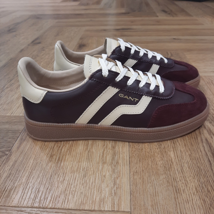 Cuzima Wine Cream Cuzima Wine Cream est un modèle d’inspiration rétro, qui se porte en toute saison. Tout d'abord, ces chaussures conçues avec une tige en cuir se distinguent par des finitions en daim lisse sur les côtés et au niveau du contrefort. Puis, la semelle extérieure en caoutchouc thermoplastique, associée à une doublure en tissu, confère un style vintage à l'ensemble. Les baskets Gant Cuzima pour femme sont la fusion parfaite entre style rétro et confort. Avec leur design intemporel et leurs matériaux de qualité supérieure, elles sont idéales pour toute occasion. Elles garantissent un look décontracté et moderne qui ne passera pas inaperçu. La marque Quand Bernard Gant, un immigrant ukrainien, arrive à New-York en 1914, il se plonge directement au cœur des métiers du prêt-à-porter. Il travaille dans un atelier de confection de chemises dans le centre de la ville. Ce n'est que quelques années plus tard, alors qu'il a déménagé à New Haven dans le Connecticut qu'il lancera l'entreprise familiale à l'aide de sa femme, également dans le métier. Rapidement, il fabrique des chemises pour les plus grandes marques du pays tel que Brooks Brothers. Si le style de Gant a beaucoup évolué au cours des années, il ne s'est jamais vraiment détaché de son image de marque Américaine traditionnelle. En effet, adepte du style Ivy avec comme produit phare la chemise à col boutonné. Après avoir été suédoise, la marque a été rachetée en 2008 par le groupe suisse Maus Frères, qui détient entre autres Lacoste et Aigle, mais elle garde encore ses valeurs originelles : celles de Bernard Gant.
