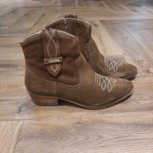 Bottines Lady Camel Bottines Lady Camel revisite l'esprit western avec élégance. Cette bottine en cuir velours séduit par sa silhouette intemporelle, ses surpiqûres décoratives et son talon biseauté qui apportent caractère et féminité à toutes vos tenues. Inspirée des incontournables santiags, la bottine LADY affirme un style authentique et raffiné. Son cuir velours souple est sublimé par des broderies graphiques sur l'avant du pied et des détails de surpiqûres contrastées. Dotée d'un talon confortable et d'une silhouette élancée, elle accompagne aussi bien un jean qu'une robe fluide pour une allure résolument tendance. Les Tropeziennes par M. Belarbi : L’histoire d’un style intemporel, né à Saint-Tropez Mo Belarbi, né à Fez, est un créateur visionnaire et passionné par le cuir, l’artisanat et les voyages. En 1975 dans le village emblématique de Saint-Tropez dont il tombe amoureux, il ouvre son premier concept store «La Puce Tropezienne», un lieu unique, foisonnant de créativité et d’audace. Mo Belarbi, esprit libre et innovant y imagine des modèles qui deviendront iconiques, intergénérationnels et s’imposeront rapidement comme incontournables.