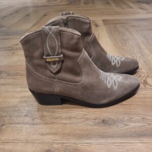 Bottines Lady Taupe Bottines Lady Taupe revisite l'esprit western avec élégance. Cette bottine en cuir velours séduit par sa silhouette intemporelle, ses surpiqûres décoratives et son talon biseauté qui apportent caractère et féminité à toutes vos tenues. Inspirée des incontournables santiags, la bottine LADY affirme un style authentique et raffiné. Son cuir velours souple est sublimé par des broderies graphiques sur l'avant du pied et des détails de surpiqûres contrastées. Dotée d'un talon confortable et d'une silhouette élancée, elle accompagne aussi bien un jean qu'une robe fluide pour une allure résolument tendance. Les Tropeziennes par M. Belarbi : L’histoire d’un style intemporel, né à Saint-Tropez Mo Belarbi, né à Fez, est un créateur visionnaire et passionné par le cuir, l’artisanat et les voyages. En 1975 dans le village emblématique de Saint-Tropez dont il tombe amoureux, il ouvre son premier concept store «La Puce Tropezienne», un lieu unique, foisonnant de créativité et d’audace. Mo Belarbi, esprit libre et innovant y imagine des modèles qui deviendront iconiques, intergénérationnels et s’imposeront rapidement comme incontournables.