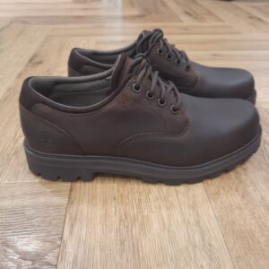 Britton Road Dark Brown Découvrez la chaussure imperméable Britton Road Dark Brown. Pour commencer, cette chaussure revisite le style Oxford décontracté. En effet, elle est équipée d’une tige en cuir Premium Timberland® Leather imperméable, d’une doublure intérieure ReBOTL™ contenant 50 % de plastique PET recyclé et d’une membrane imperméable TimberDry™. Puis, elle possède une assise plantaire en mousse à mémoire de forme OrthoLite® pour garder vos pieds au sec et parfaitement amortis. De plus, sa semelle extérieure crantée TimberGrip™ offre une adhérence optimale sur tous types de surfaces. L’histoire de Timberland L’histoire des Timberland Boots remonte à la ville de Newmarket, dans le New Hampshire, aux États-Unis, où elles ont été créées en 1973. À l’origine, elles étaient destinées aux travailleurs du bâtiment et des espaces extérieurs. Les fondateurs, Nathan Swartz et sa famille, ont mis l’accent sur la qualité et la durabilité dès le départ. C’est ainsi que les premières Timberland Boots sont nées, dotées de coutures étanches, d’une semelle crantée pour une meilleure adhérence, et d’un cuir de première qualité. Cette combinaison de caractéristiques en a rapidement fait des chaussures de choix pour les travailleurs et les amateurs de plein air. Au fil des années, les Timberland Boots ont conquis un public plus large. Elles sont devenues un élément essentiel du style urbain.  Notamment dans le mouvement hip-hop des années 90, où elles ont été adoptées comme symbole de résilience et de style. Le nom « Timberland » lui-même évoque des images de forêts, de montagnes et d’aventures en plein air. Effectivement, cela en fait un choix idéal pour les esprits aventuriers.