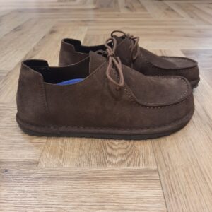 Utti Lace Chocolat La BIRKENSTOCK Utti Lace Chocolat est une chaussure intemporelle aux allures de mocassin. Le petit plus : sa couture qui ne passe pas inaperçue. En plus d’offrir un confort optimal, la languette de talon permet d’enfiler et de retirer la chaussure très facilement. L’histoire de Birkenstock Tout commence en 1774, lorsque Johann Adam Birkenstock, un cordonnier allemand passionné, fonde ce qui allait devenir l'une des marques de chaussures les plus emblématiques au monde. À l'époque, Johann menait une petite entreprise modeste qui lui permettait de vivre confortablement. Mais comment cette production familiale a-t-elle pu se transformer en un empire mondial de la chaussure ? Le tournant se produit en 1896 avec Konrad Birkenstock, un descendant de la famille. Konrad, visionnaire, décide de donner un coup de jeune à l'entreprise familiale. C'est lui qui a développé la première semelle intérieure orthopédique, une innovation qui a littéralement mis le sabot Birkenstock sur la carte mondiale. Cependant, il aura fallu plusieurs générations et une évolution constante pour que Birkenstock devienne la marque internationale que l'on connaît aujourd'hui. Le grand bond en avant s’est produit au XXe siècle, notamment aux États-Unis dans les années 1960, où les sandales Birkenstock sont devenues un symbole de la contre-culture et du confort.