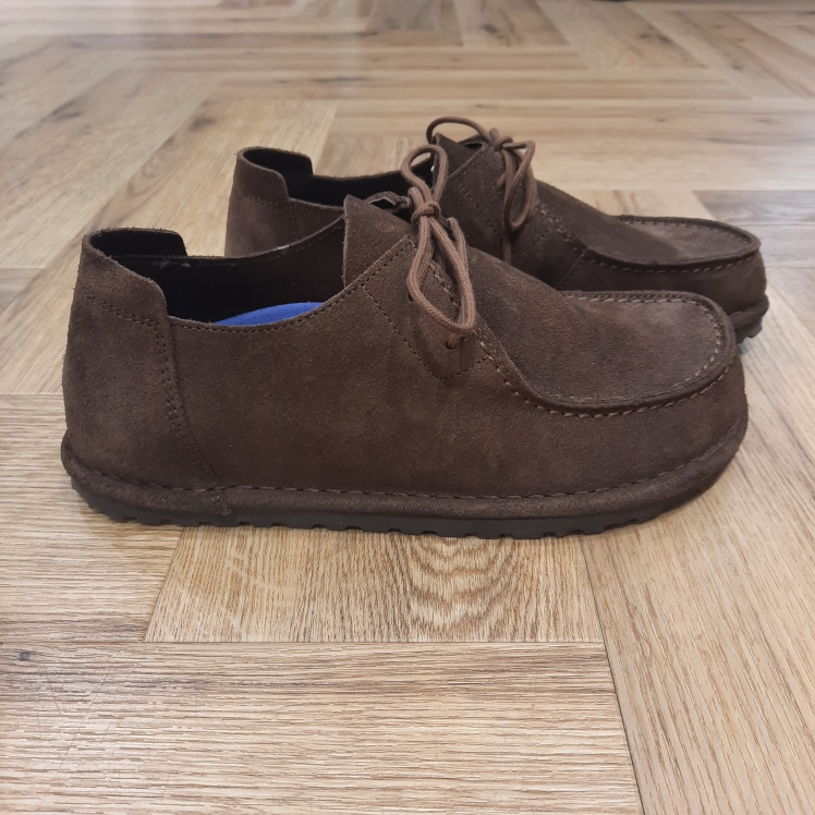 Utti Lace Chocolat La BIRKENSTOCK Utti Lace Chocolat est une chaussure intemporelle aux allures de mocassin. Le petit plus : sa couture qui ne passe pas inaperçue. En plus d’offrir un confort optimal, la languette de talon permet d’enfiler et de retirer la chaussure très facilement. L’histoire de Birkenstock Tout commence en 1774, lorsque Johann Adam Birkenstock, un cordonnier allemand passionné, fonde ce qui allait devenir l'une des marques de chaussures les plus emblématiques au monde. À l'époque, Johann menait une petite entreprise modeste qui lui permettait de vivre confortablement. Mais comment cette production familiale a-t-elle pu se transformer en un empire mondial de la chaussure ? Le tournant se produit en 1896 avec Konrad Birkenstock, un descendant de la famille. Konrad, visionnaire, décide de donner un coup de jeune à l'entreprise familiale. C'est lui qui a développé la première semelle intérieure orthopédique, une innovation qui a littéralement mis le sabot Birkenstock sur la carte mondiale. Cependant, il aura fallu plusieurs générations et une évolution constante pour que Birkenstock devienne la marque internationale que l'on connaît aujourd'hui. Le grand bond en avant s’est produit au XXe siècle, notamment aux États-Unis dans les années 1960, où les sandales Birkenstock sont devenues un symbole de la contre-culture et du confort.